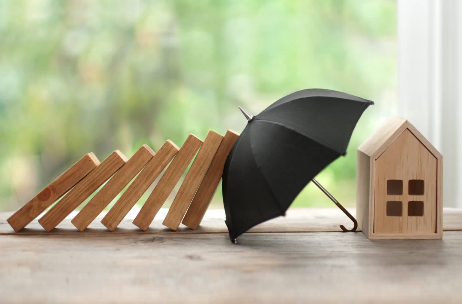 Umbrella protecting house from domino collapse, insurance concept